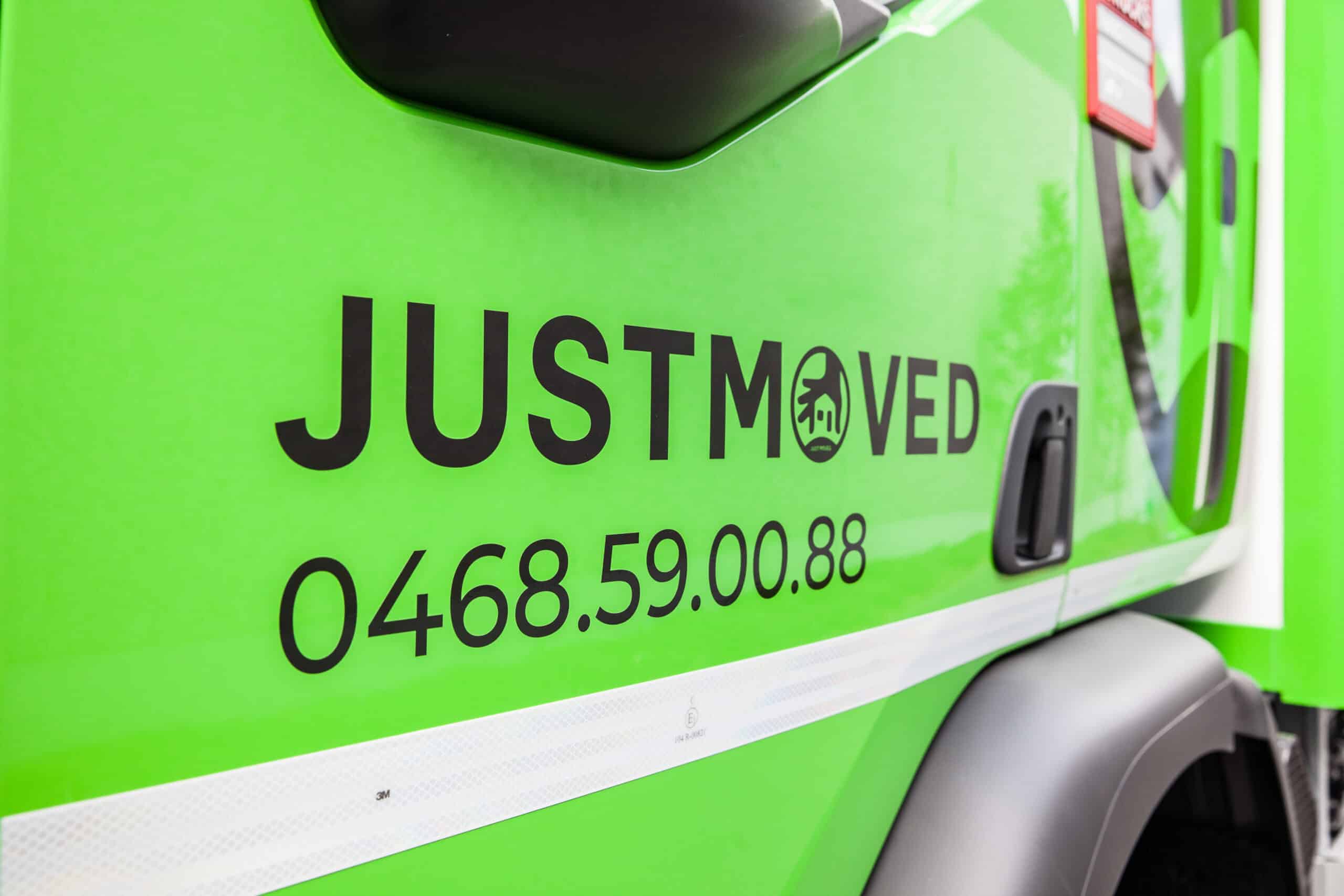 Green moving truck with JUST MOVED branding and contact details.